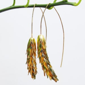 May include: A pair of gold dangle earrings with a wheat-like design. The earrings are made of thin wire and have a long, flowing shape.
