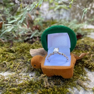 May include: A green velvet ring box shaped like a turtle with a silver ring with a large emerald-cut diamond inside.