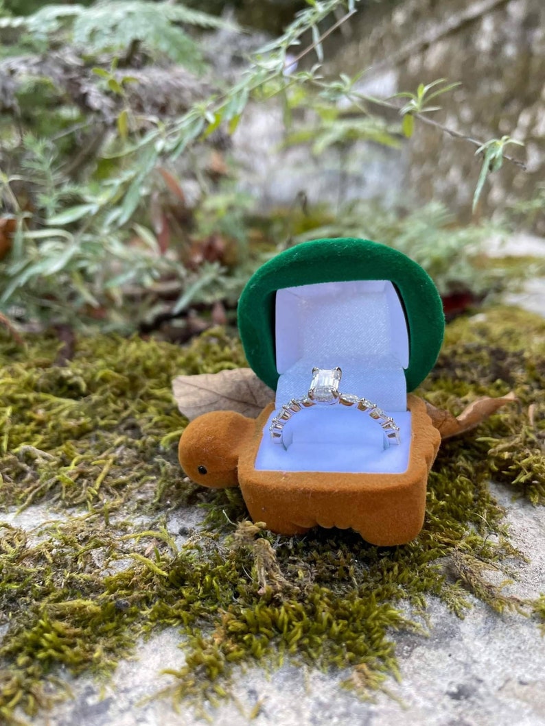 May include: A green velvet ring box shaped like a turtle with a silver ring with a large emerald-cut diamond inside.