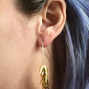 May include: Gold dangle earrings with a cascading design of small, overlapping leaves. The earrings are long and delicate, with a simple wire hook.