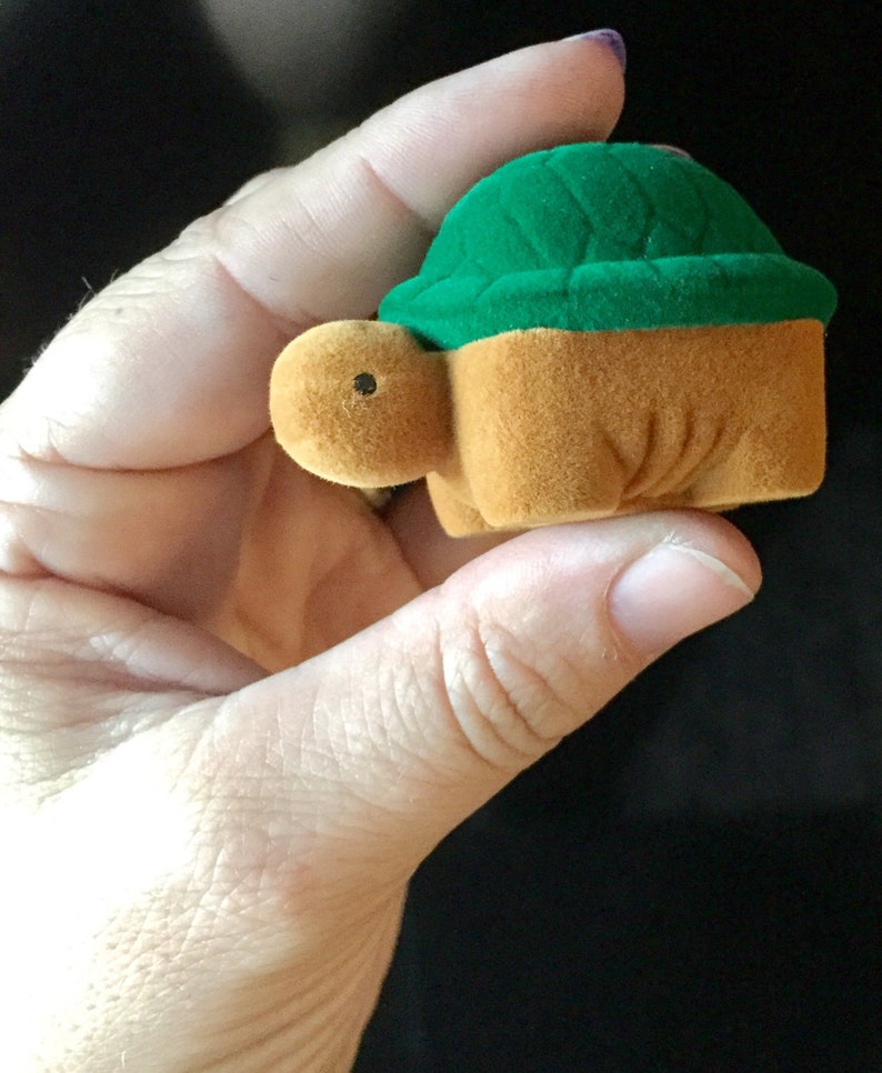 May include: A small, brown and green turtle-shaped ring box. The box is made of velvet and has a green lid.