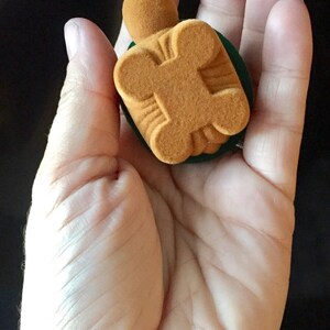 May include: A small, brown velvet ring box with a green velvet lining. The box is shaped like a turtle.