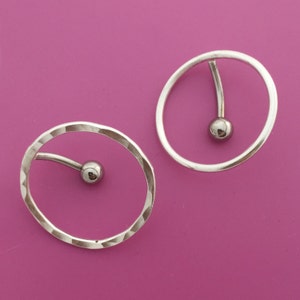 Puede incluir: Dos pendientes de aro de plata con una pequeña bola de plata en el extremo de una barra curva que atraviesa el aro.