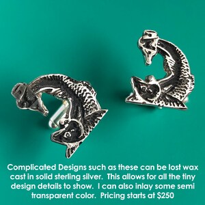 May include: A pair of silver cufflinks featuring a detailed design of two fish intertwined. The cufflinks are cast in solid sterling silver.