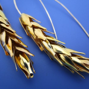 May include: A pair of gold wheat-shaped earrings with silver hooks. The earrings are made of multiple small, overlapping pieces of metal that resemble wheat stalks.