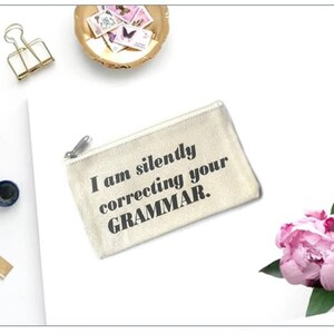 May include: A white canvas zippered pouch with the text "I am silently correcting your GRAMMAR." printed in black.