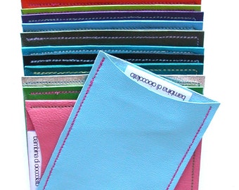 May include: A stack of colorful leather wallets with a light blue wallet on top. The light blue wallet has a pink stitched border and a white label that says "bambina di cioccolato".