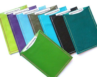 May include: A set of eight leather card holders in various colors, including green, purple, blue, black, and teal. Each holder has a stitched edge and a small pocket on the front.