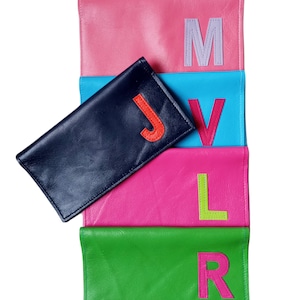 Puede incluir: Cinco bolsas de cuero en diferentes colores con una sola letra en cada una. Las letras son J, V, L, R y M. Las letras son de diferentes colores y están cosidas en las bolsas.