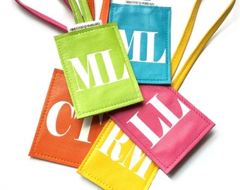 May include: Five colourful leather luggage tags with white letters spelling out the word "MIL" on three of the tags and "RM" and "IL" on the other two tags.