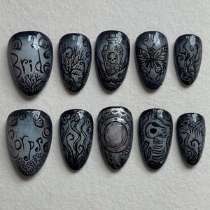 May include: A set of ten press-on nails featuring a grey and black gradient base with intricate hand-painted designs including the words Bride and Corpse, a skull in a bottle, a butterfly, seaweed, a porthole, a skeleton, and a fish skeleton.