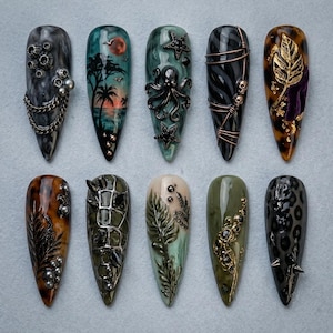 May include: Ten almond-shaped press-on nails featuring diverse 3D designs including a sunset palm tree landscape, a black octopus, gold leaf accents, metallic chains, skulls, leopard print, and botanical leaf motifs in various dark and earthy tones.