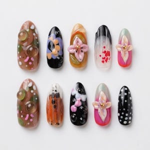 Peut inclure: Un ensemble de dix faux ongles présentant des motifs variés, notamment marron avec des sphères translucides en relief, noir avec des accents floraux violets, ambre avec des fleurs roses en 3D, blanc avec des éclaboussures rouges et noir à pois blancs.