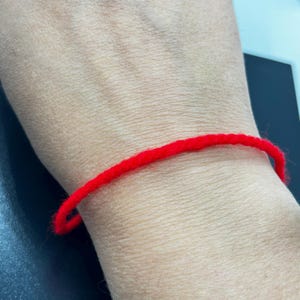 May include: A red string bracelet worn on a person's wrist.