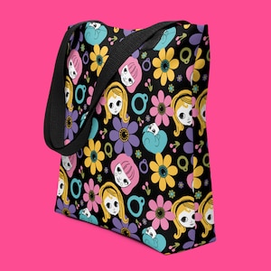 May include: Black tote bag with a colorful pattern of flowers and cartoon faces. The flowers are pink, yellow, purple, and blue. The faces are of girls with long eyelashes and blonde hair.