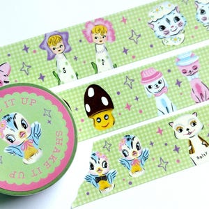 May include: Decorative washi tape roll and strips featuring whimsical illustrations. The tape roll has a green and pink design with a bird graphic and the text "SHAKE IT UP". The strips have repeating patterns of cartoon characters, stars, and a green gingham background.