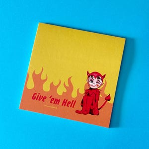 May include: A square notepad with a yellow top and orange bottom featuring a graphic of a red devil character winking. The design includes orange flame illustrations and the red text Give 'em Hell printed on the lower left side of the paper.
