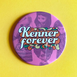 May include: Pink round button with a retro design featuring a group of dolls and the text "Kenner forever".