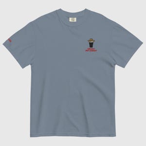 Op de afbeelding: Lichtblauw T-shirt met een geborduurd ontwerp van een cowboyhoed op een pintglas. De tekst "CREAMY PINT COWBOY" is rood. Het shirt heeft een ronde hals en korte mouwen, ideaal voor casual wear.