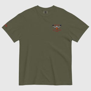 Puede incluir: Camiseta verde oliva con un peque&ntilde;o gr&aacute;fico de un toro con sombrero de vaquero y dos jarras de cerveza. El texto "Sip the Legend" y "For a Legendary Pint" est&aacute; debajo. Un peque&ntilde;o logotipo rojo est&aacute; en la manga izquierda.