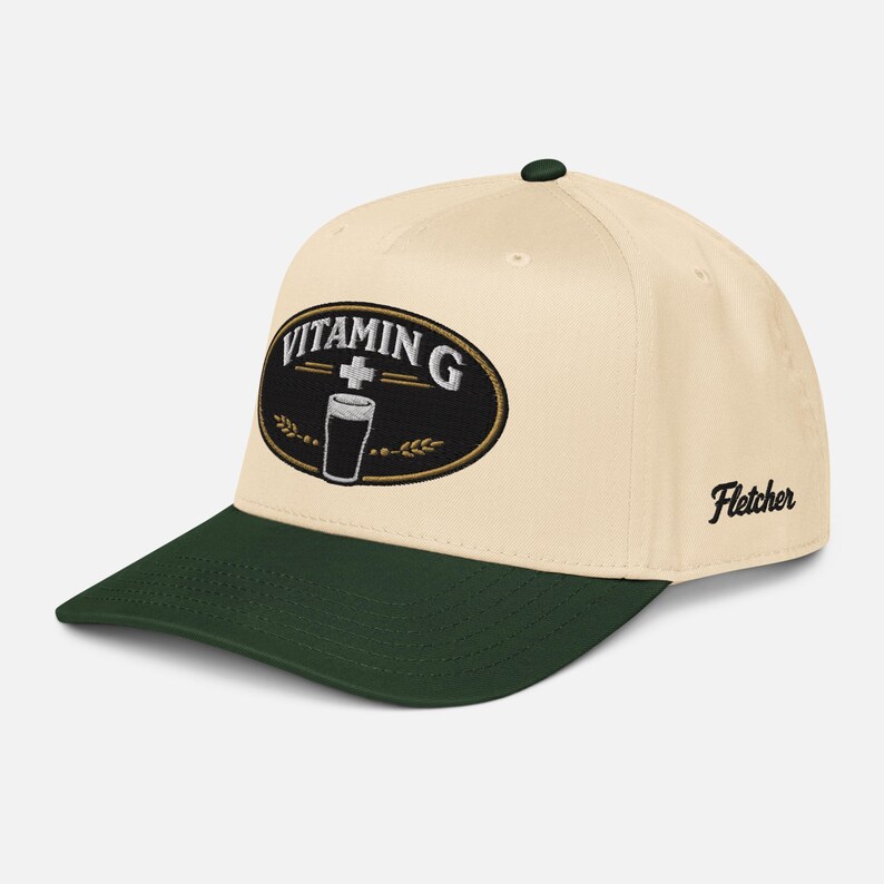 Puede incluir: Gorra de b&eacute;isbol color crema con visera y bot&oacute;n superior verde oscuro. La gorra presenta un parche ovalado bordado con las palabras "Vitamin G" y un vaso de cerveza. El nombre "Fletcher" est&aacute; bordado en el lateral.