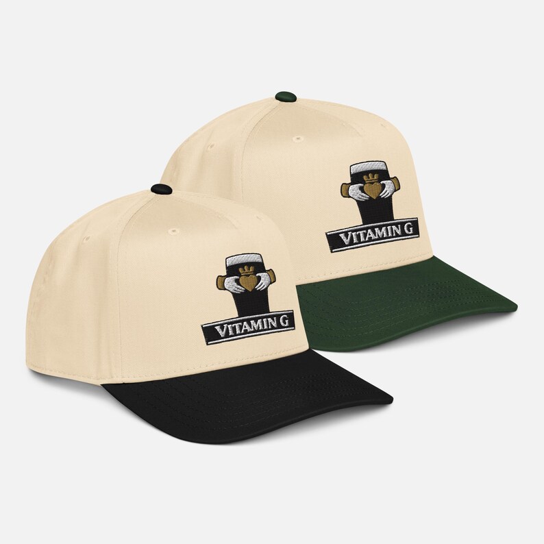 May include: Two baseball caps with a cream-colored crown and a black brim. Each cap features an embroidered logo of a beer glass with a heart and the text "VITAMIN G" in a black rectangle. One cap has a green brim.