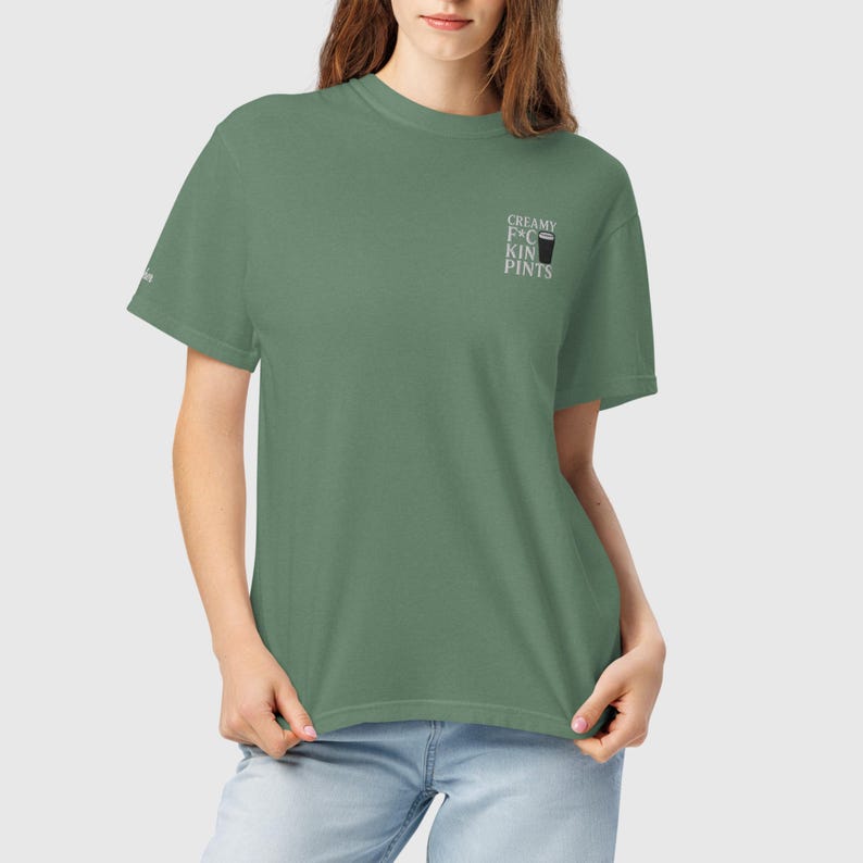 K&ouml;nnte beinhalten: Salbeigr&uuml;nes T-Shirt mit dem Text "CREAMY F*CKIN PINTS" und einer kleinen Grafik eines Bierglases. Das Shirt hat eine lockere Passform und kurze &Auml;rmel. Der Text ist in Wei&szlig; gehalten.