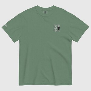 K&ouml;nnte beinhalten: Salbeigr&uuml;nes T-Shirt mit dem Text "CREAMY F*CKIN PINTS" und einer kleinen Grafik eines Bierglases. Das Shirt besteht aus einem weichen Material und hat einen klassischen Rundhalsausschnitt. Das Shirt hat eine lockere Passform.