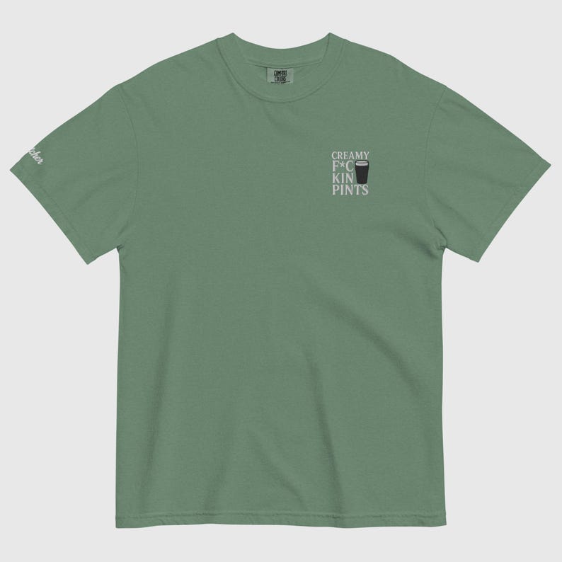 K&ouml;nnte beinhalten: Salbeigr&uuml;nes T-Shirt mit dem Text "CREAMY F*CKIN PINTS" und einer kleinen Grafik eines Bierglases. Das Shirt besteht aus einem weichen Material und hat einen klassischen Rundhalsausschnitt. Das Shirt hat eine lockere Passform.