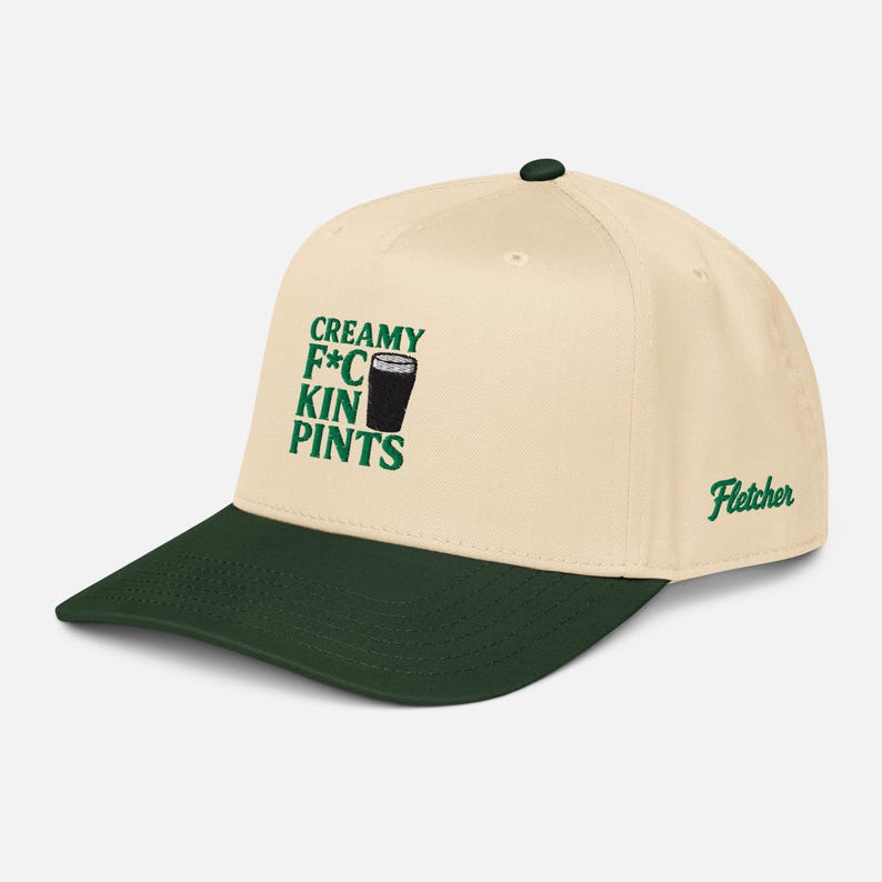 Puede incluir: Gorra de b&eacute;isbol crema con visera y bot&oacute;n verde oscuro. La gorra presenta el texto "CREAMY F*CKIN PINTS" en verde, junto con un gr&aacute;fico de una pinta de cerveza. El nombre "Fletcher" est&aacute; bordado en el lateral.