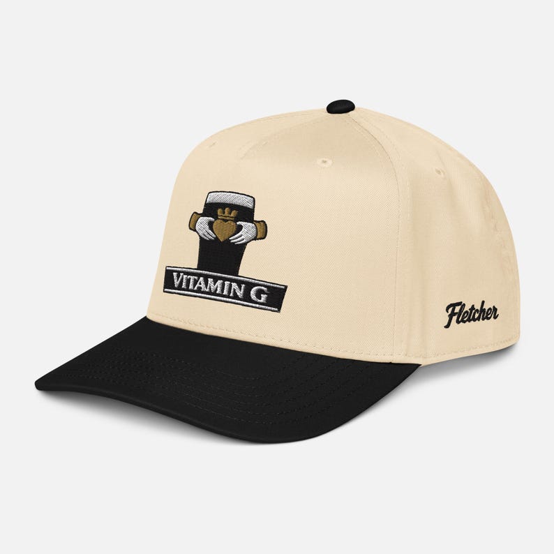 May include: Cream-colored baseball cap with a black brim. The cap features an embroidered design of a beer glass with a heart and hands, and the text "Vitamin G" on a black rectangle. The name "Fletcher" is embroidered on the side.