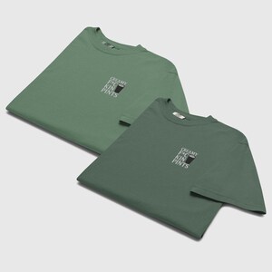 K&ouml;nnte beinhalten: Zwei gr&uuml;ne T-Shirts, eines etwas heller als das andere, werden gezeigt. Jedes Shirt hat den wei&szlig;en Text "CREAMY F*CKIN PINTS" &uuml;ber einer schwarzen Grafik. Die Shirts sind gefaltet und flach ausgelegt.