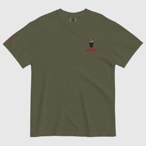 Op de afbeelding: Olijfgroen t-shirt met een kleine afbeelding van een cowboyhoed op een donkere drank, en de rode tekst "Cowboy Pint Always". Het shirt is effen van kleur en heeft een relaxte pasvorm.