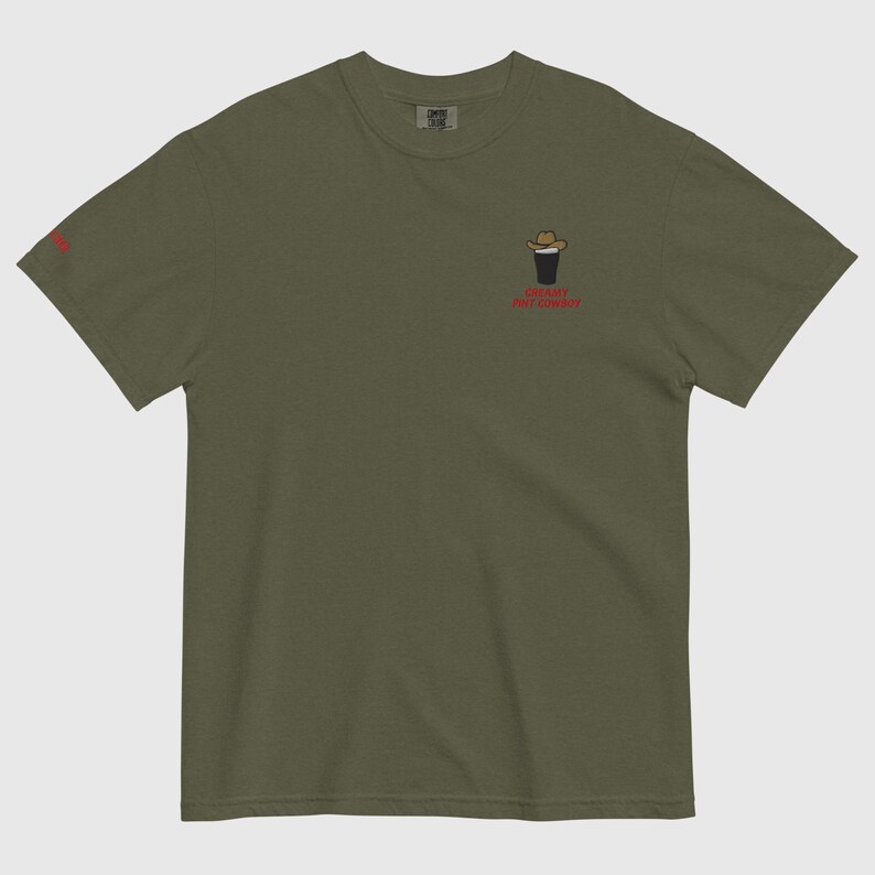 Op de afbeelding: Olijfgroen t-shirt met een kleine afbeelding van een cowboyhoed op een donkere drank, en de rode tekst "Cowboy Pint Always". Het shirt is effen van kleur en heeft een relaxte pasvorm.