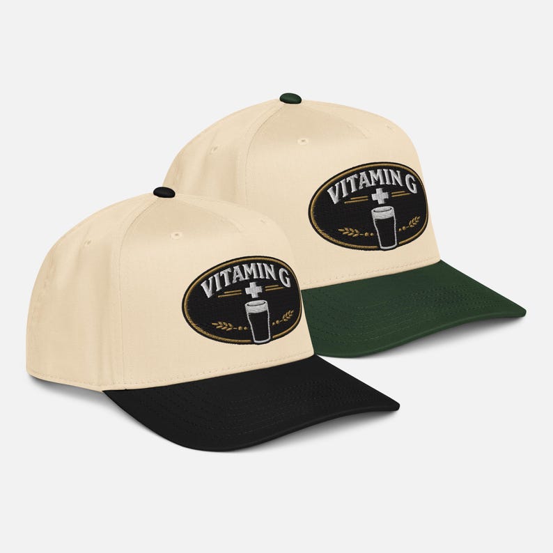 Puede incluir: Dos gorras de b&eacute;isbol con corona color crema y visera negra. Cada gorra presenta un parche ovalado con las palabras "VITAMIN G" sobre un vaso y un s&iacute;mbolo de cruz. Una gorra tiene visera verde.