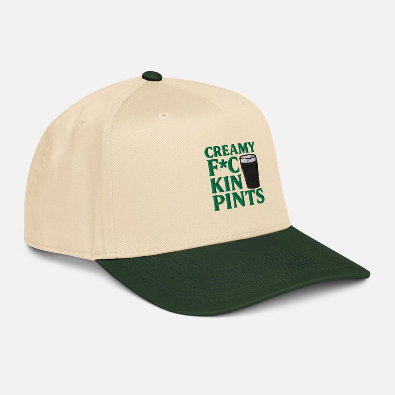 Puede incluir: Gorra de b&eacute;isbol color crema con visera verde oscuro. La gorra presenta el texto "CREAMY F*CKIN PINTS" en verde, con un gr&aacute;fico de una pinta de cerveza negra. Un accesorio casual y elegante.