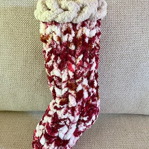 May include: A red and white knitted Christmas stocking with a white fluffy cuff. The stocking is made of a soft, fuzzy yarn.