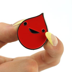 May include: Red enamel pin shaped like a smiling blood drop.