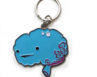 May include: A light blue brain-shaped keychain with a silver key ring. The brain has a black eye and mouth, with pink and purple swirls on the right side. The keychain is made of metal.