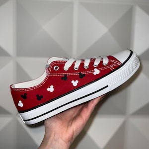 May include: Red canvas low-top trainers with white laces and black and white Mickey Mouse heads printed on the red canvas.