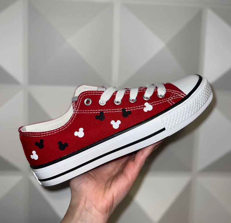 May include: Red canvas low-top trainers with white laces and black and white Mickey Mouse heads printed on the red canvas.