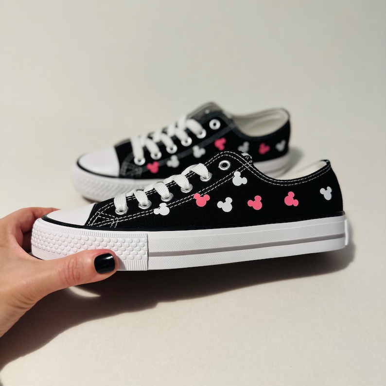 May include: Black canvas sneakers with white and pink Mickey Mouse silhouettes printed all over.