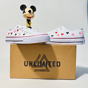 May include: White canvas shoes with red and black Mickey Mouse heads printed on them. The shoes are sitting on a box that says "UNLIMITED 777".