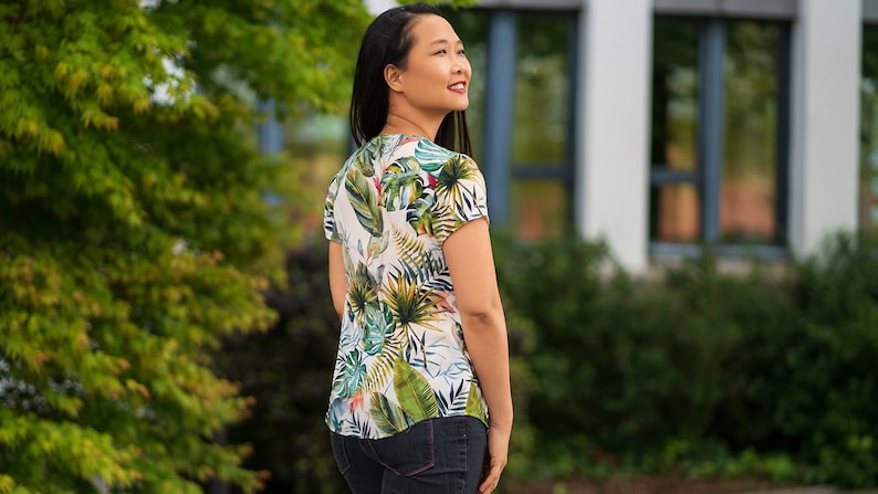 May include: A white blouse with a tropical print featuring green, blue, and yellow leaves. The blouse has a V-neck and short sleeves.