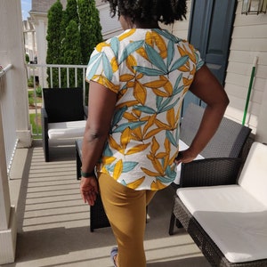 May include: A person wearing a white and yellow short-sleeved shirt with a blue and yellow leaf pattern. The person is wearing brown pants and blue shoes.