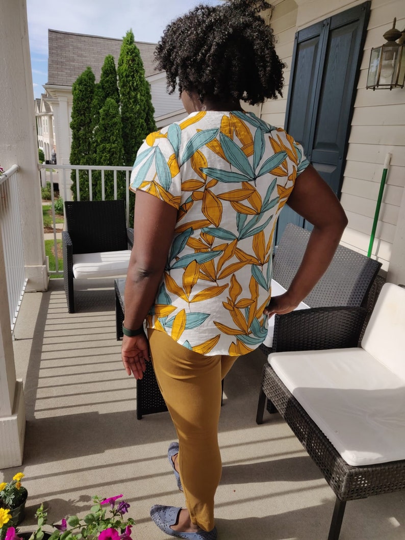 May include: A person wearing a white and yellow short-sleeved shirt with a blue and yellow leaf pattern. The person is wearing brown pants and blue shoes.