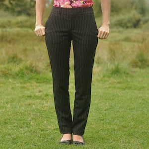 May include: A woman wearing black pinstripe pants with a black belt.