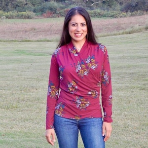 May include: A woman wearing a long-sleeved, burgundy floral print blouse with a V-neck and blue jeans.