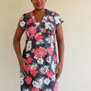 May include: A woman wearing a short-sleeved black dress with a floral print. The dress has a V-neck and a relaxed fit. The flowers are red, white, and green.