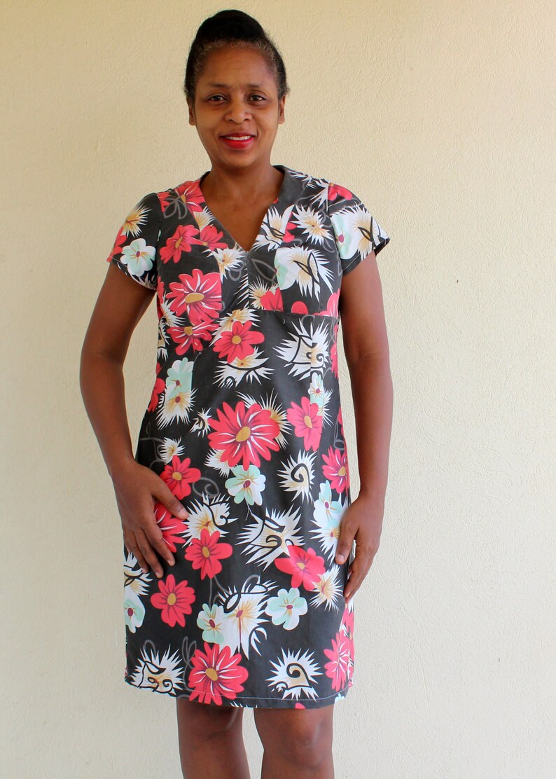May include: A woman wearing a short-sleeved black dress with a floral print. The dress has a V-neck and a relaxed fit. The flowers are red, white, and green.
